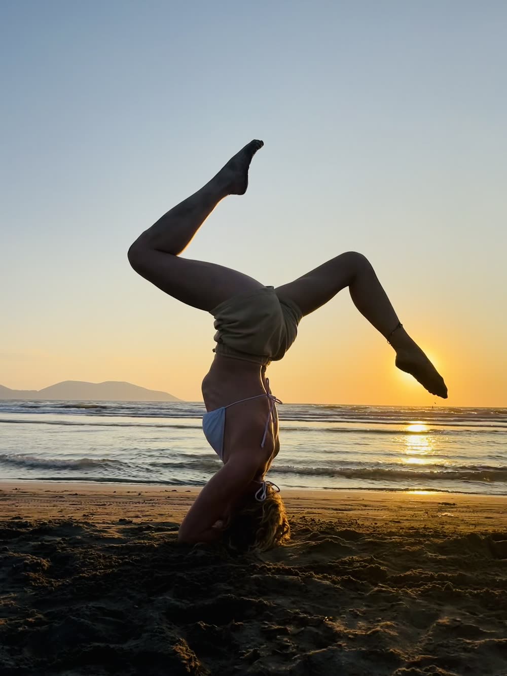 Silueta haciendo el pino sobre las manos en la playa al atardecer