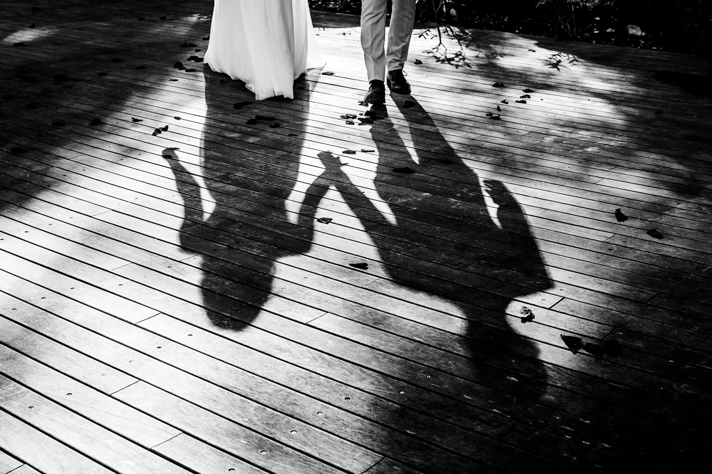 Silhouettes of a couple holding hands, cast as shadows on a wooden deck